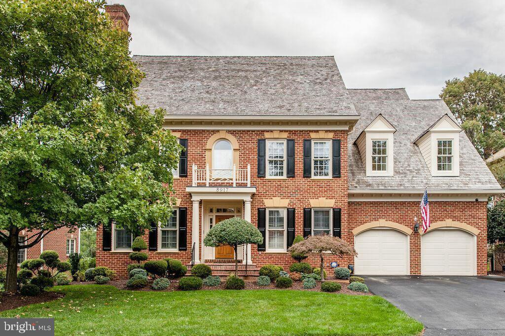 colonial inspired home featuring brick siding, a front lawn, aphalt driveway, a garage, and a balcony