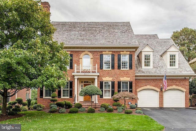 colonial-style house with brick siding, aphalt driveway, a front yard, a garage, and a balcony