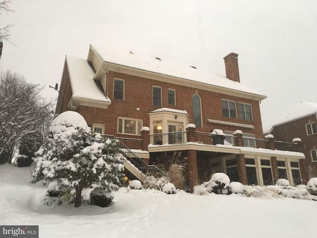 snow covered back of property featuring stairway, brick siding, and a chimney