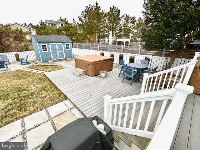 1 E Essex St, Fenwick Island, DE 19944 - wooden terrace featuring a hot tub, outdoor dining space, a fenced backyard, a storage unit, and an outbuilding