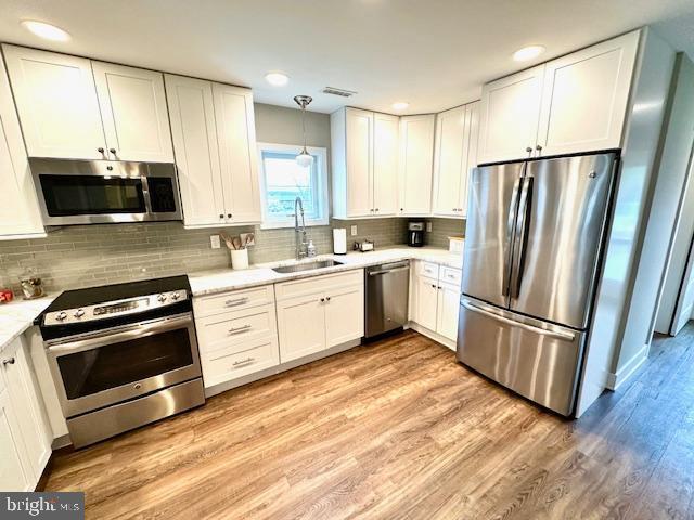1 E Essex St, Fenwick Island, DE 19944 - kitchen featuring stainless steel appliances, a sink, white cabinets, light countertops, and light wood-style floors
