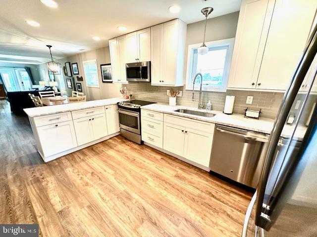 1 E Essex St, Fenwick Island, DE 19944 - kitchen with stainless steel appliances, a sink, a peninsula, light countertops, and light wood-style flooring
