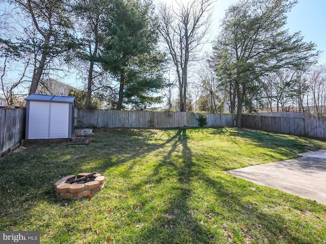 view of yard featuring an outbuilding, a storage unit, a fenced backyard, and a fire pit