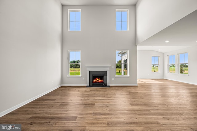 unfurnished living room with a fireplace with flush hearth, baseboards, and wood finished floors