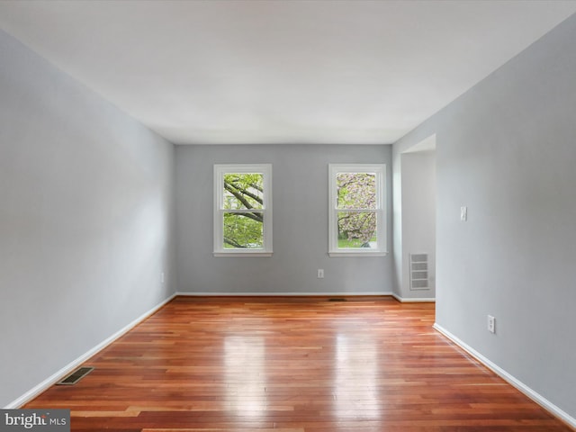 empty room featuring wood-type flooring, visible vents, and baseboards