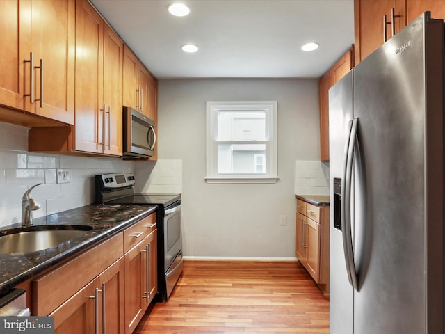 kitchen featuring light wood-style flooring, brown cabinetry, appliances with stainless steel finishes, a sink, and backsplash