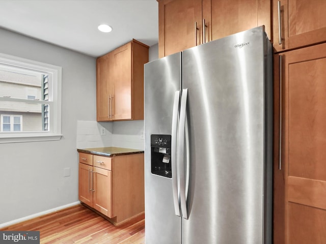kitchen with brown cabinetry, light wood-type flooring, baseboards, and stainless steel fridge