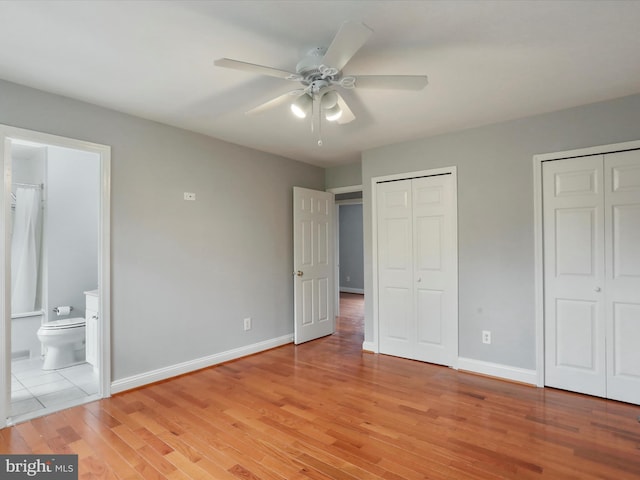 unfurnished bedroom featuring baseboards, connected bathroom, multiple closets, ceiling fan, and light wood finished floors