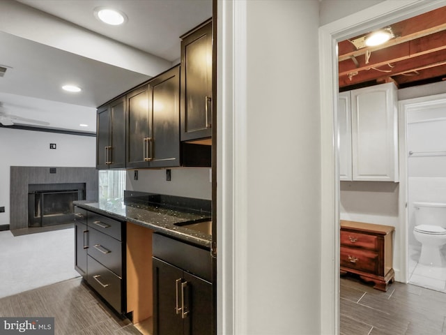kitchen featuring visible vents, a sink, a fireplace, recessed lighting, and dark stone counters