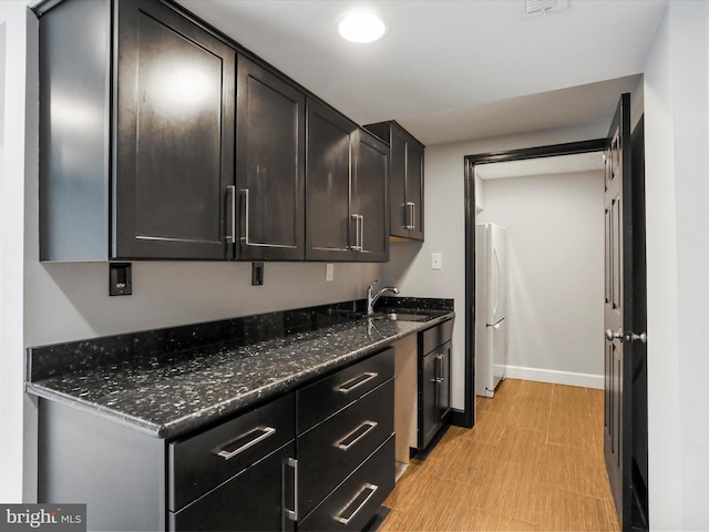 kitchen with baseboards, freestanding refrigerator, a sink, and dark stone counters