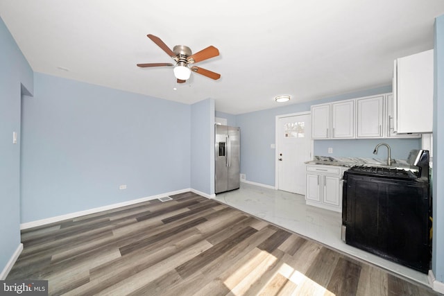 kitchen featuring baseboards, gas range, stainless steel fridge, white cabinetry, and a ceiling fan