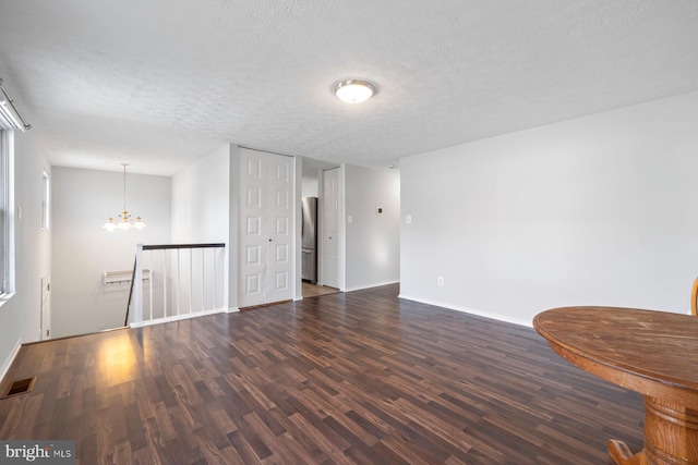 empty room featuring visible vents, a textured ceiling, wood finished floors, an inviting chandelier, and baseboards