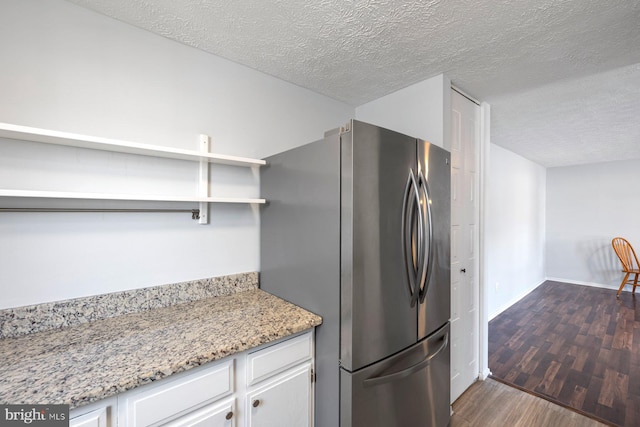 kitchen with dark wood finished floors, white cabinets, freestanding refrigerator, and a textured ceiling