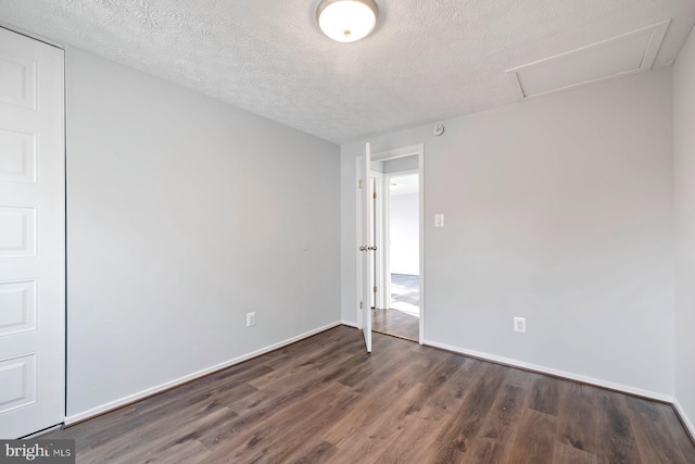 empty room with a textured ceiling, attic access, baseboards, and wood finished floors