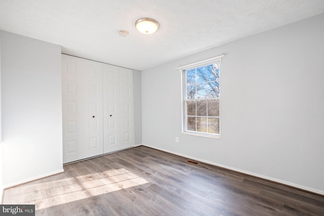 unfurnished bedroom with visible vents, a textured ceiling, wood finished floors, a closet, and baseboards