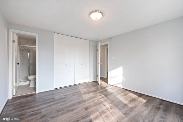 unfurnished bedroom with a closet, ensuite bathroom, baseboards, and wood finished floors