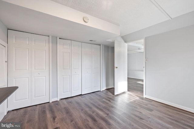 unfurnished bedroom with baseboards, two closets, and dark wood-style floors