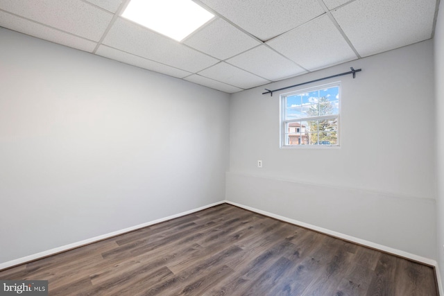 spare room featuring baseboards, a paneled ceiling, and wood finished floors