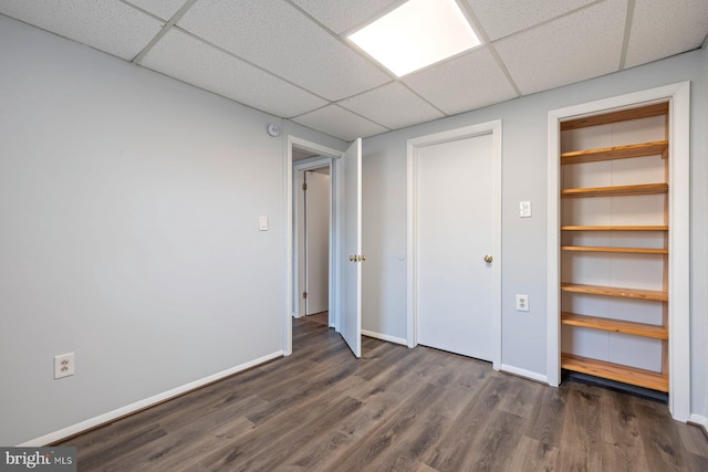 unfurnished bedroom with dark wood finished floors, a drop ceiling, and baseboards