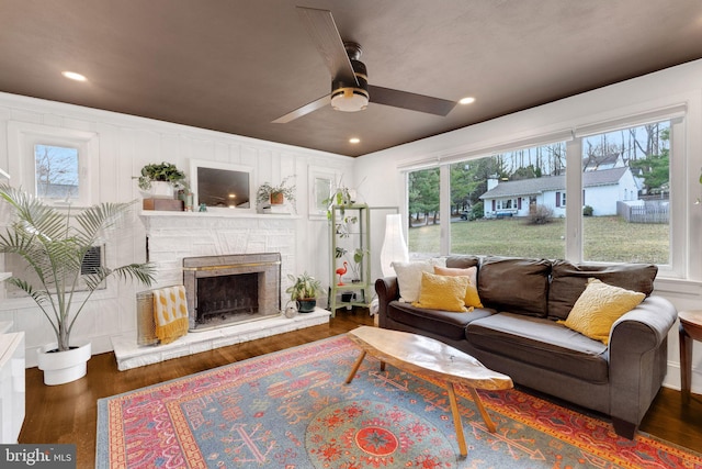 living area featuring ceiling fan, a stone fireplace, recessed lighting, wood finished floors, and a decorative wall