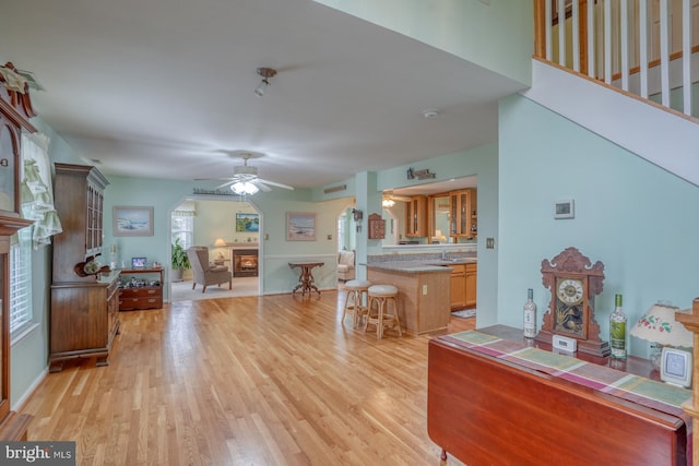 interior space featuring a ceiling fan, a fireplace, light wood-type flooring, and arched walkways