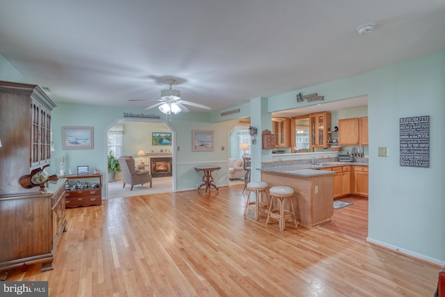 kitchen featuring a ceiling fan, a breakfast bar, arched walkways, a sink, and light wood-type flooring