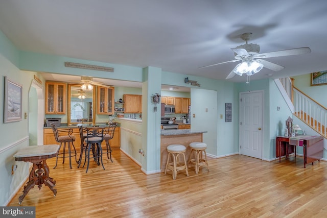 kitchen featuring glass insert cabinets, light wood finished floors, a ceiling fan, and appliances with stainless steel finishes