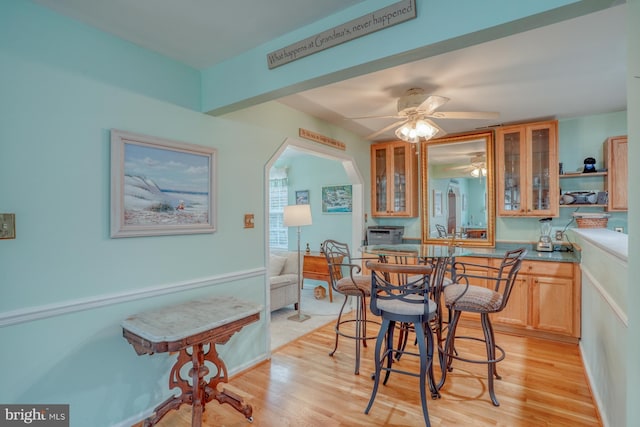 dining room with arched walkways, a ceiling fan, and light wood-style floors