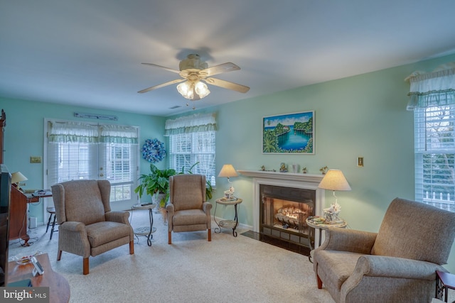 carpeted living area with a fireplace with flush hearth and a ceiling fan