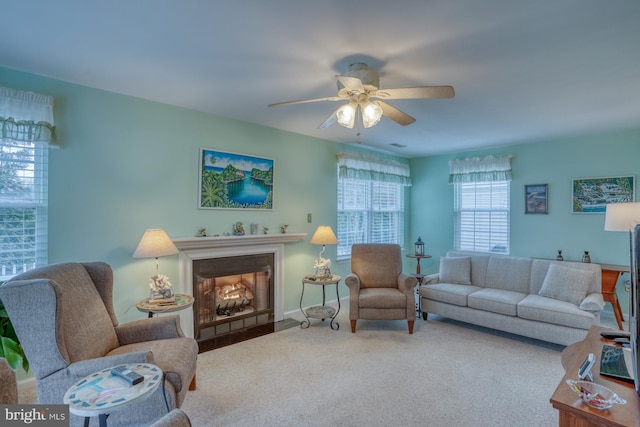 living area featuring a fireplace with flush hearth, ceiling fan, and carpet flooring