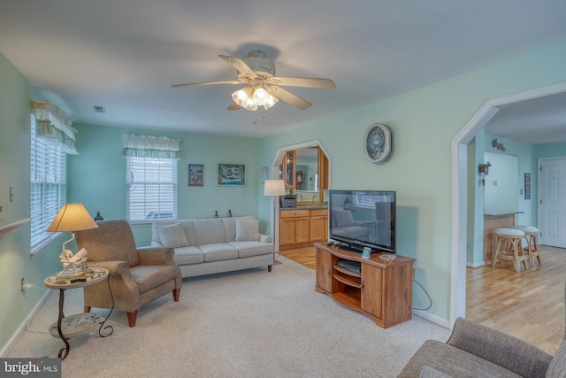 living room featuring light carpet, visible vents, baseboards, and ceiling fan