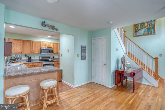 kitchen featuring baseboards, a kitchen bar, light wood-style floors, stainless steel appliances, and a sink