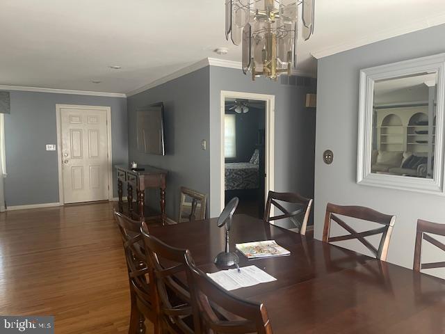 dining room with baseboards, wood finished floors, ornamental molding, and ceiling fan with notable chandelier