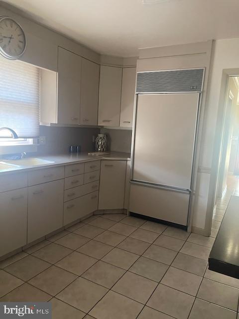 kitchen featuring light countertops, light tile patterned flooring, white cabinetry, paneled refrigerator, and a sink