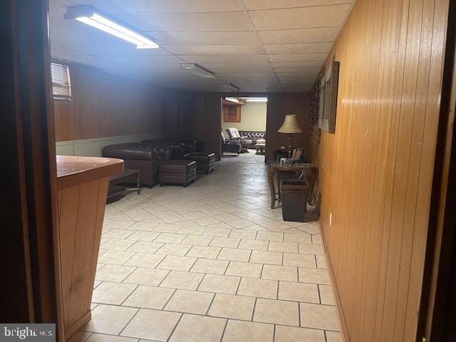 hallway with light tile patterned floors, a drop ceiling, and wood walls