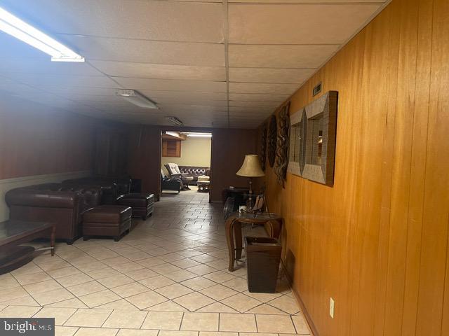 hall with light tile patterned flooring, wooden walls, and a drop ceiling