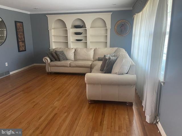 living area featuring built in shelves, wood finished floors, baseboards, visible vents, and crown molding