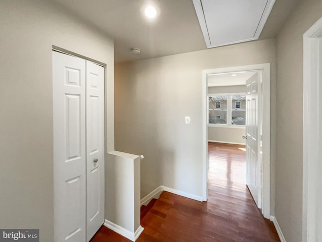 corridor featuring an upstairs landing, attic access, baseboards, and wood finished floors