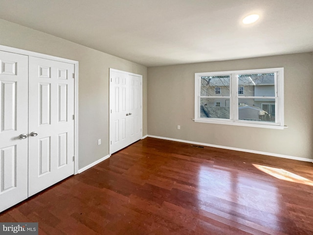 unfurnished bedroom featuring visible vents, baseboards, two closets, and wood finished floors