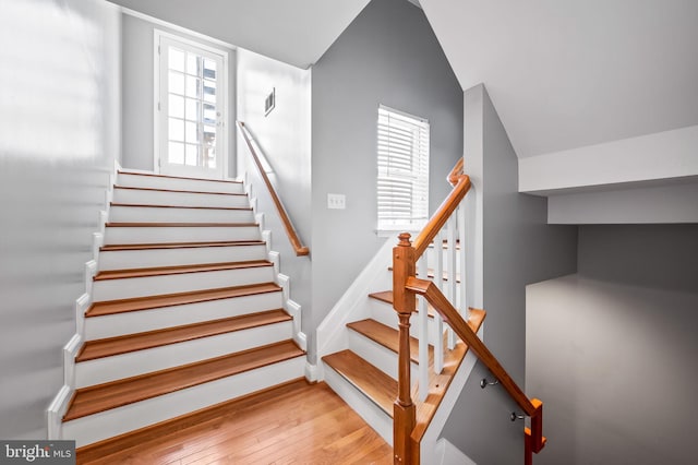 stairs with vaulted ceiling, visible vents, baseboards, and hardwood / wood-style floors