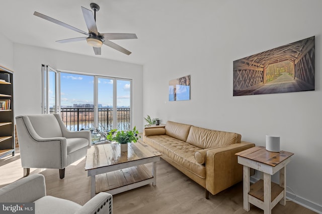 living area with a ceiling fan, wood finished floors, a water view, and baseboards