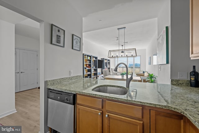 kitchen with light wood-type flooring, brown cabinets, a sink, light stone countertops, and dishwasher