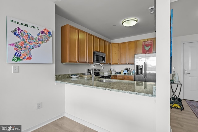 kitchen featuring light stone counters, a peninsula, light wood-style flooring, a sink, and appliances with stainless steel finishes