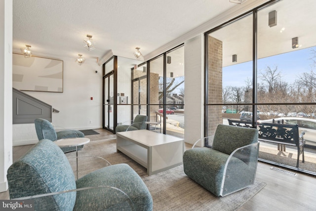 living area with visible vents, baseboards, a wall of windows, wood finished floors, and a textured ceiling