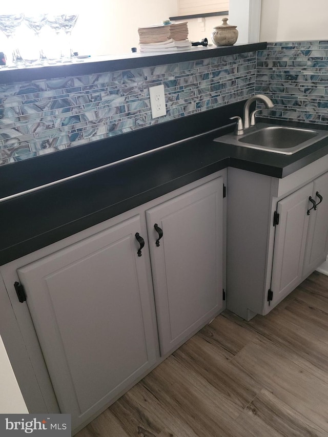 kitchen with a sink, wood finished floors, dark countertops, and white cabinets