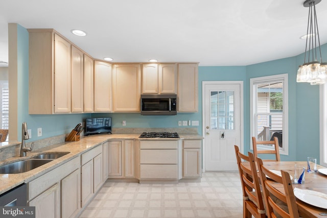 kitchen featuring stainless steel microwave, light stone countertops, light floors, black gas stovetop, and a sink