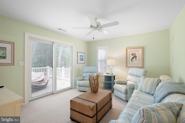 living area with plenty of natural light, light colored carpet, visible vents, and ceiling fan