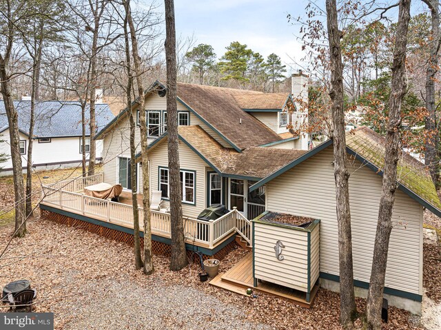 rear view of property featuring a chimney, a deck, and roof with shingles