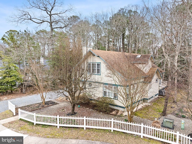 shingle-style home with central air condition unit, a fenced front yard, and a shingled roof