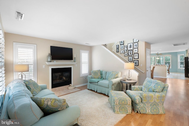 living area featuring visible vents, a fireplace with flush hearth, wood finished floors, and stairs